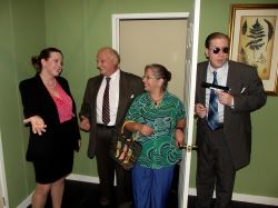 Accountant Karen Brown (Shirley Panek) welcomes Mayor Meekly and his wife Mary (Ken Kienas and Rachel Duda) to her motel room while the Mayor's security guard Agent Frank (Eric Small) prepares to protect the two of them.