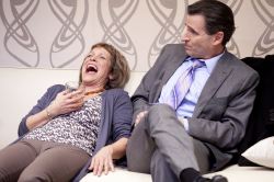 Veronica Novak (Naomi Jacobson) laughs as she may have had one too many, as Alan Raleigh (Paul Morella) looks on.